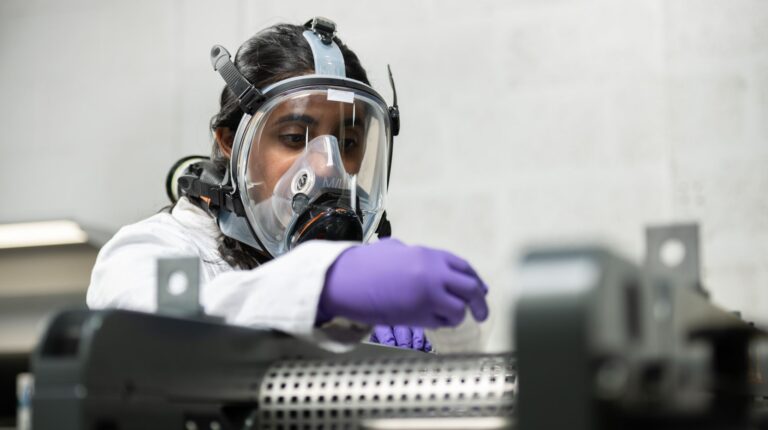Anaphite secures £1.4m funding to advance LFP dry-coating technology Anaphite battery scientist testing a dry coating precursor powder in a multi-roll calender. They are wearing white overalls, a gas mask and purple gloves
