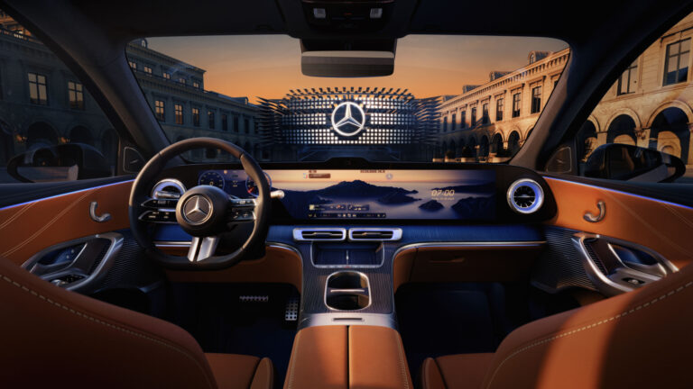 The inside of a Mercdes-Benz EV, with a light bron seating and a dark grey dash. A cityscape at dusk stretches out beyond the windshield.
