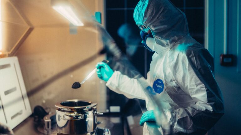 An EV battery engineer in a white laboartory suit and protective mouth and face covering carries out material tests.
