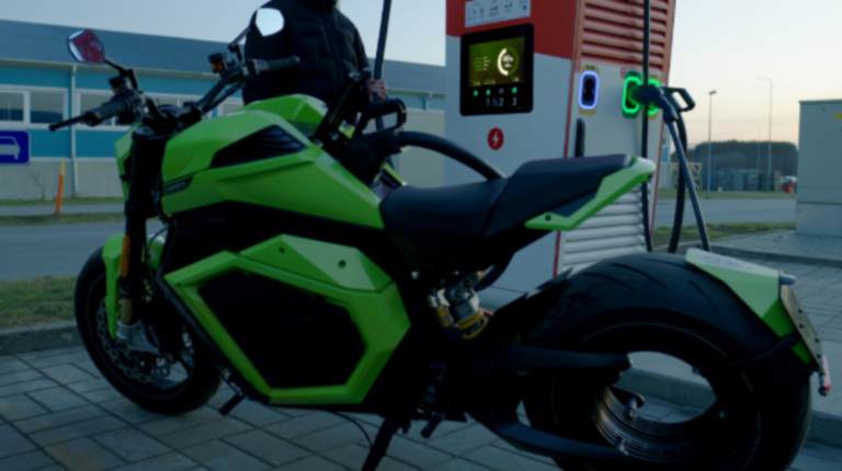 A green and black Verge TS Pro motorcycle at a charging point at a gas station.