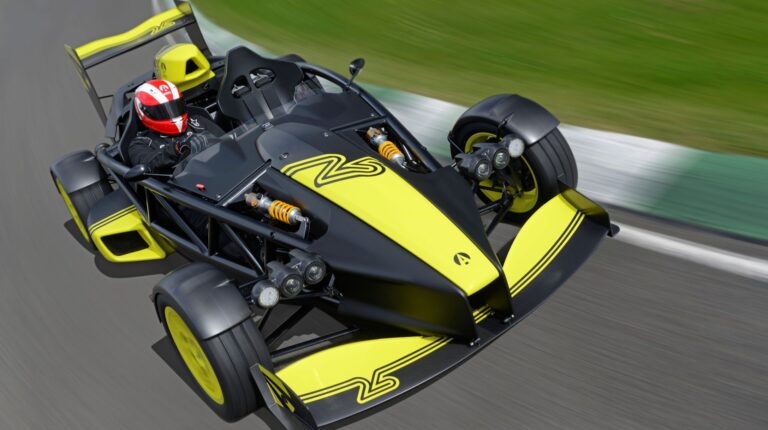 The Ariel Atom 4RR in black and yellow livery drives at high speed on a race track.