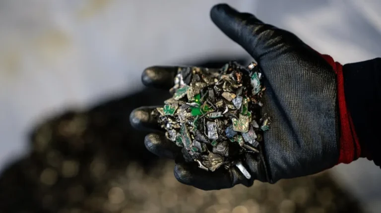 A black-gloved hand holds battery waste waiting to be recycled.