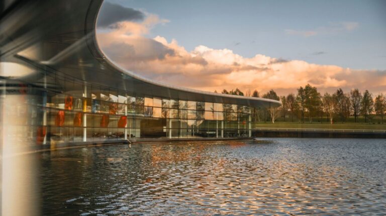External view of the McLaren Production Centre in Woking, UK, with glass offices and a water feature.