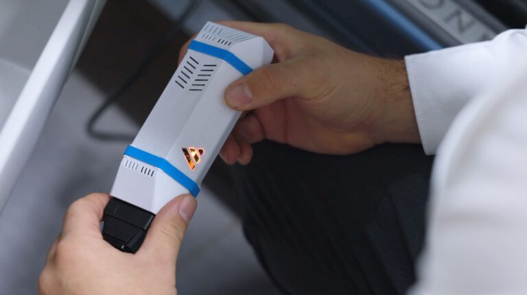 Aviloo launches independent study into used EV battery health An EV technician wearing a white laboratory coat and holding a small grey testing device carries out an AVILOO Flash Test.