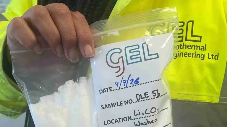 A person wearing a yellow high vis jacket holds up a plastic bag containing a lithium sample. The bag has GEL written on it.